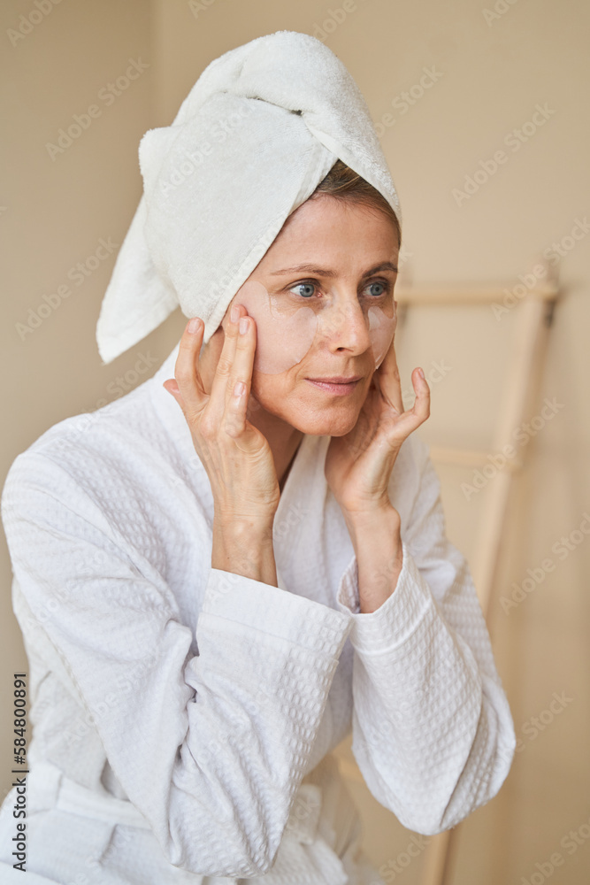 Woman in towel and bathrobe applying face patches Woman in towel and bathrobe applying face patches