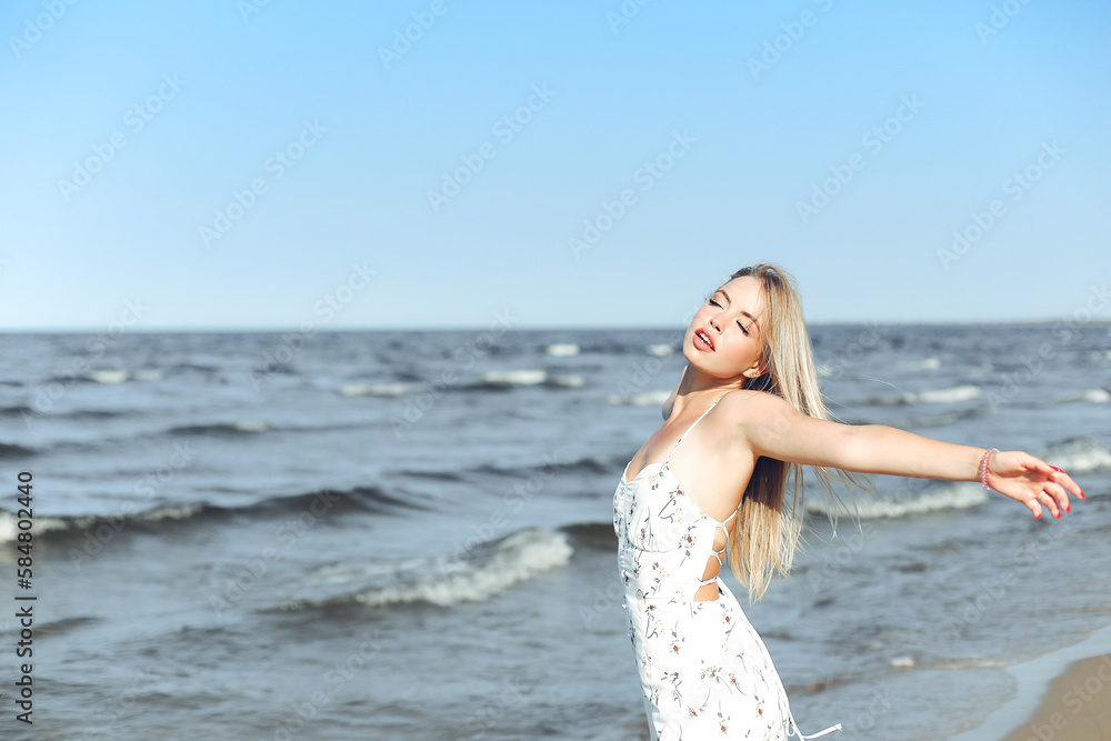 Happy blonde beautiful woman on the ocean beach standing in a white summer dress, open arms Happy blonde beautiful woman on the ocean beach standing in a white summer dress, open arms