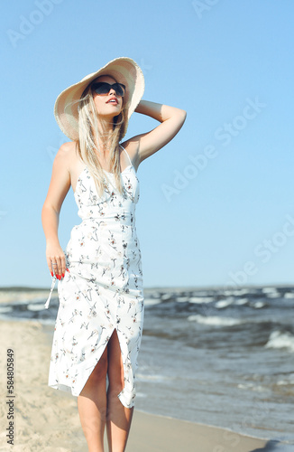Happy blonde woman in free happiness bliss on ocean beach standing with sun glasses and hat