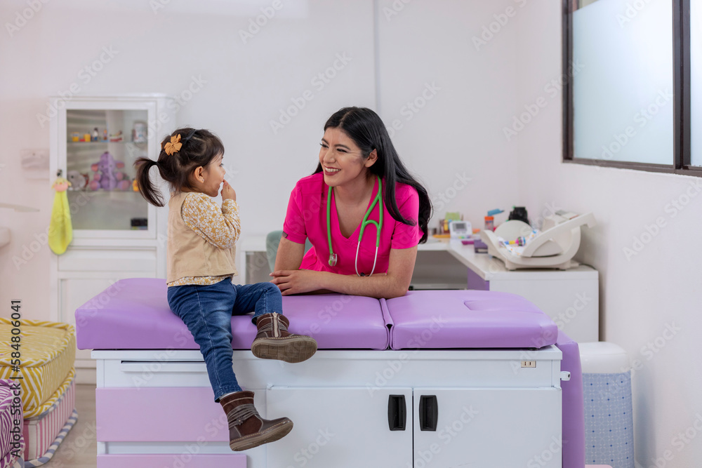 Female pediatrician smiling while looking at a little girl in her medical office