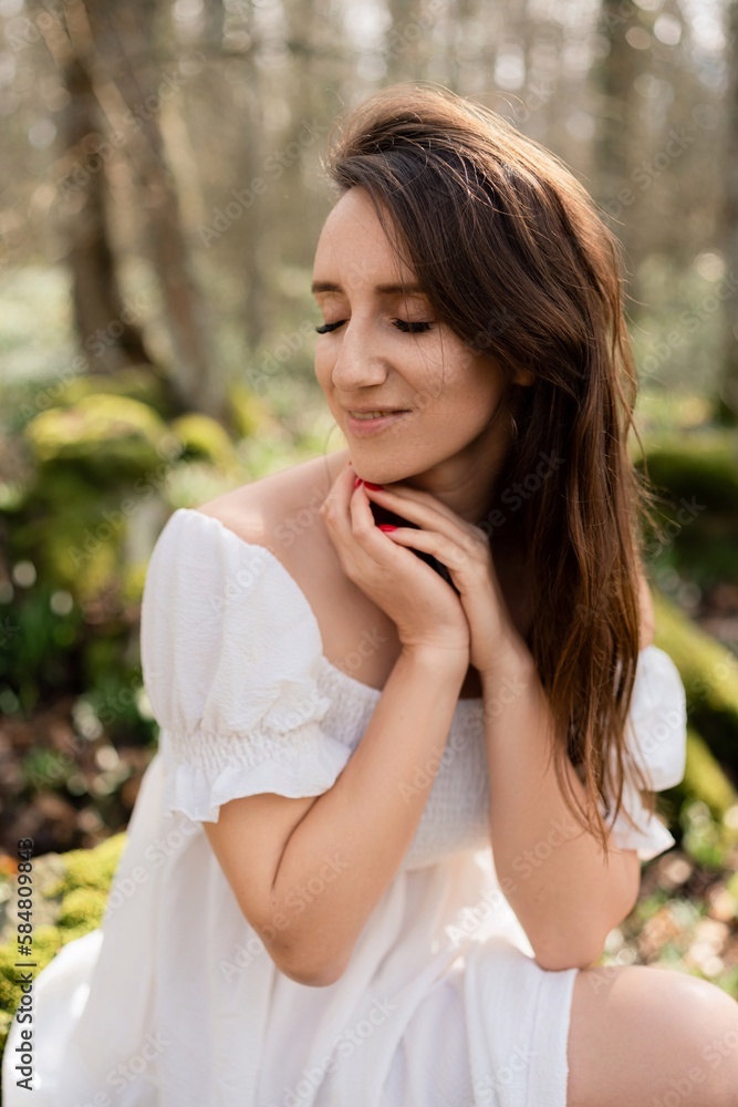 Portrait of a woman in the forest. She is sitting in a white dress on a meadow with snowdrops in a spring forest Portrait of a woman in the forest. She is sitting in a white dress on a meadow with snowdrops in a spring forest