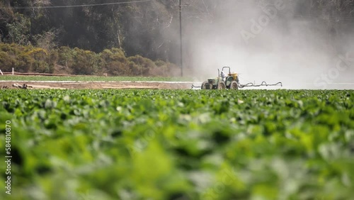 2022 - Distant view of a tractor spraying pesticide on a California farm.