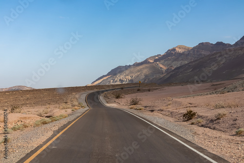 Panoramic view of endless empty road leading to colorful geology of multi hued Artist Palette rock formations in Death Valley National Park near Furnace Creek, California, USA. Black mountains