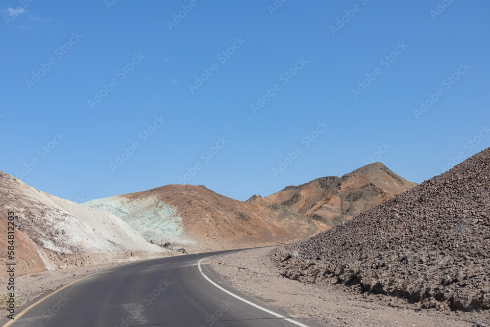 Panoramic view of endless empty road leading to colorful geology of multi hued Artist Palette rock formations in Death Valley National Park near Furnace Creek, California, USA. Black mountains Panoramic view of endless empty road leading to colorful geology of multi hued Artist Palette rock formations in Death Valley National Park near Furnace Creek, California, USA. Black mountains