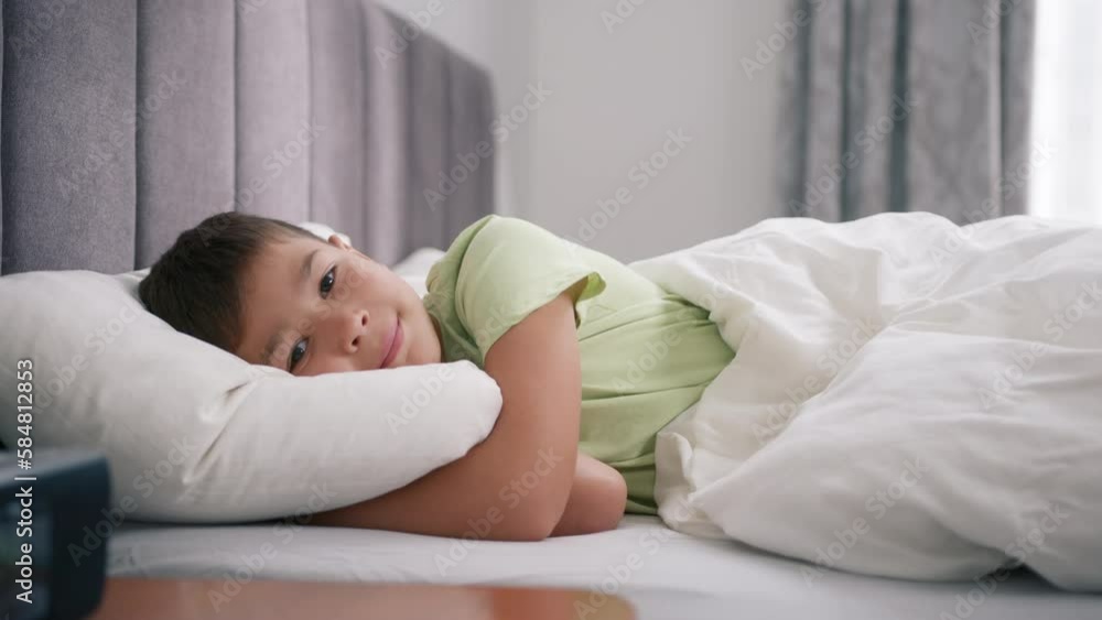 Video Stock Happy boy hugs pillow smiling, lying in comfortable bed on ...