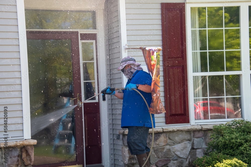 A caucasian man with a latex holding water sprayer wand power washing the front of a house A caucasian man with a latex holding water sprayer wand power washing the front of a house