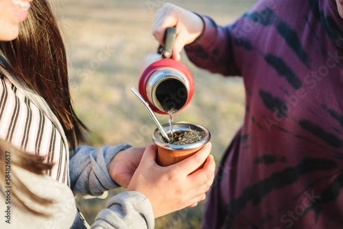Bild auf Leinwand Two female friends brewing and drinking yerba mate, with a red thermos, in the c