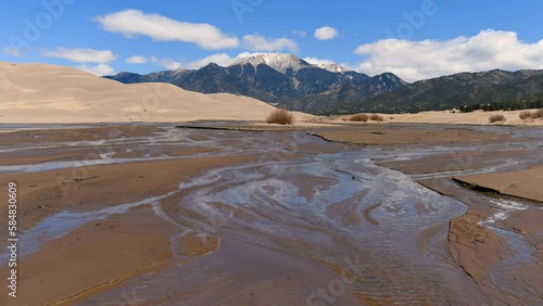 Spring Medano Creek - A sunny Spring day view of Medano Creek, with white clouds flying over rolling Great Sand Dunes and snow-capped Mt. Herard in background. Great Sand Dunes National Park, CO, USA. photo