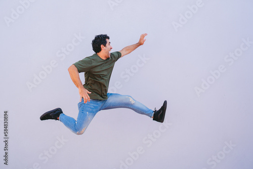Middle-aged latin man in jeans jumping excitedly on a white background. Copy space.