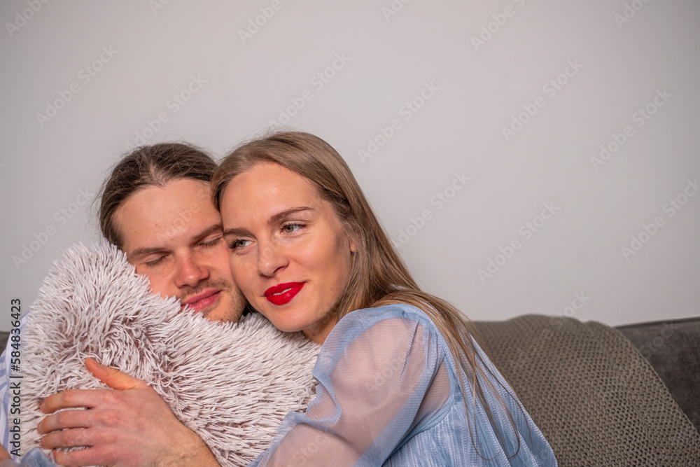 The young smiling couple in love caressing a fluffy light gray pillow,. The joy of being together. The young smiling couple in love caressing a fluffy light gray pillow,. The joy of being together.