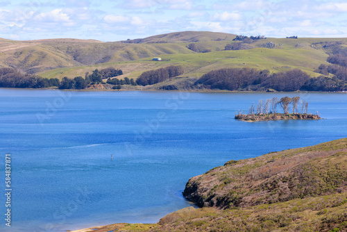 Small island in blue waters and rolling green hills on California coast