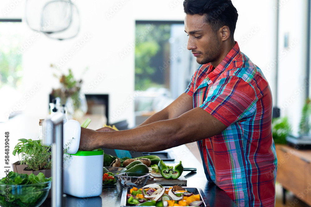 Happy biracial man preparing dinner, chopping vegetables and composting waste in kitchen Happy biracial man preparing dinner, chopping vegetables and composting waste in kitchen