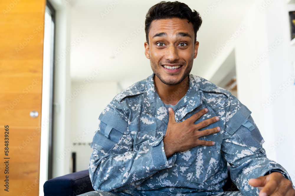Happy biracial male soldier wearing uniform, sitting in armchair making video call at home Happy biracial male soldier wearing uniform, sitting in armchair making video call at home