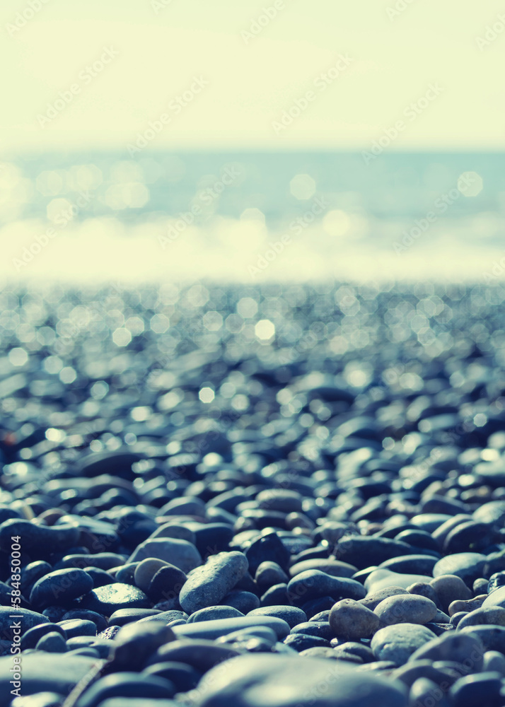 Obraz premium Marine background. Pebble beach on a sunny day. Pebbles close-up, sea and sky in summer without people, soft selective focus 