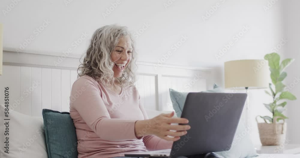 Happy senior caucasian woman sitting on bed making video call on laptop and waving, slow motion Happy senior caucasian woman sitting on bed making video call on laptop and waving, slow motion