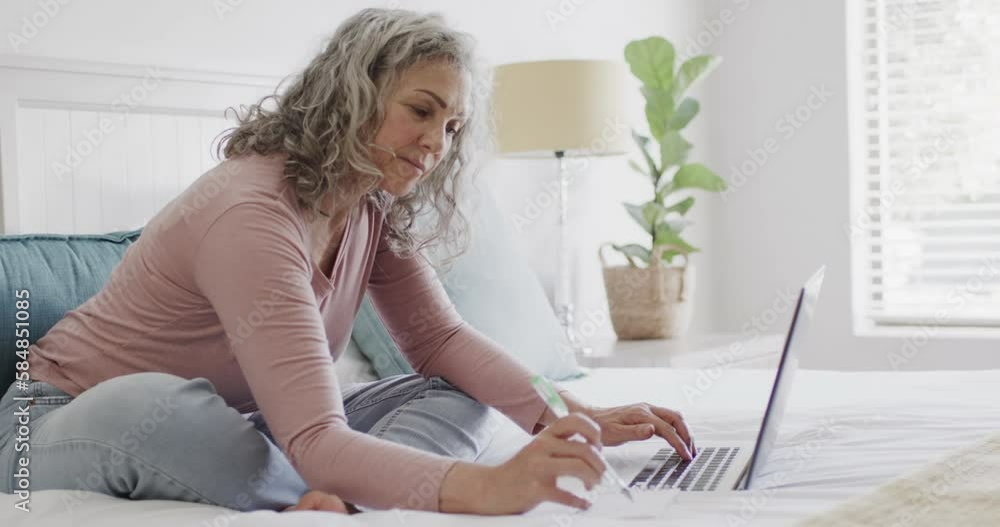 Happy senior caucasian woman sitting on bed and using laptop, slow motion Happy senior caucasian woman sitting on bed and using laptop, slow motion