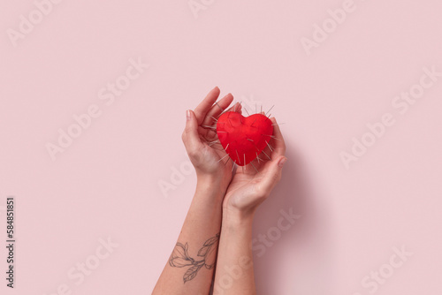 Red heart with thorns in tattooed woman's hands.