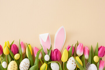 Easter idea. Top view photo of rabbit bunny ears pink yellow tulips flowers and colorful easter eggs on isolated beige background with empty space