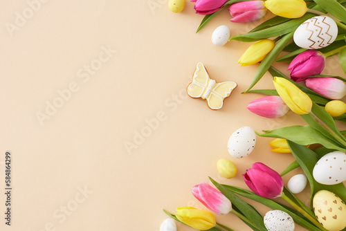 Easter decor concept. Top view composition of colorful easter eggs yellow pink tulips flowers and butterfly cookie on isolated beige background with copyspace