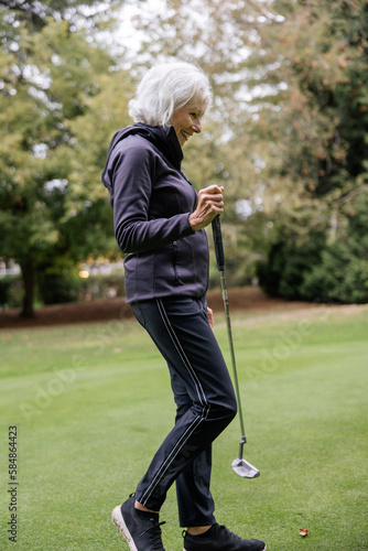 Grey haired woman walking holding golf clubs on course. photo