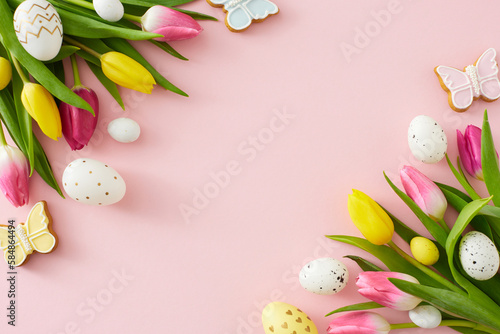 Easter decorations concept. Flat lay photo of yellow white easter eggs tulips flowers and butterfly cookies on pastel pink background with empty space in the middle. Holiday card idea