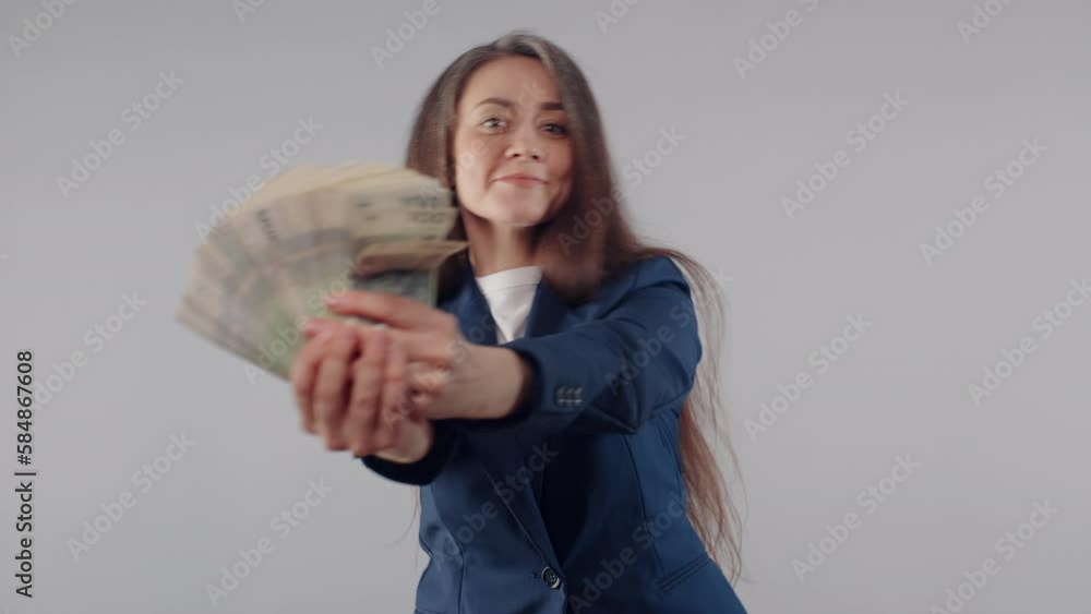 Funny attractive caucasian business woman in blue jacket holding stack of money banknotes bills in her hands standing on grey background, joyful female office manager smiles enjoying cash income Funny attractive caucasian business woman in blue jacket holding stack of money banknotes bills in her hands standing on grey background, joyful female office manager smiles enjoying cash income
