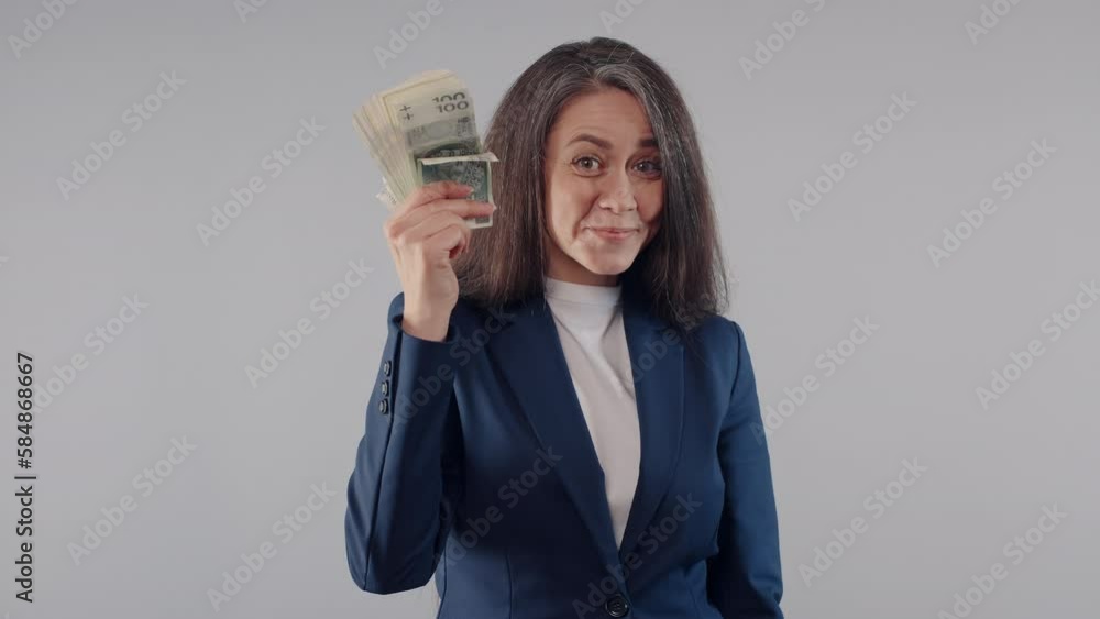 Beautiful caucasian business woman in blue jacket shows and waving stack of money banknotes bills in her hand standing on grey background, joyful female office manager smiles posing with cash income Beautiful caucasian business woman in blue jacket shows and waving stack of money banknotes bills in her hand standing on grey background, joyful female office manager smiles posing with cash income