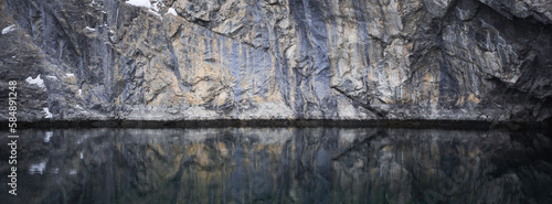 A rock face is reflected in water.