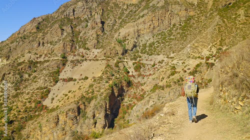 Backpacking trekker walking on dusty mountainous trail toward snowy mountain peaks and valleys in the far distance, Annapurna, Nepal Backpacking trekker walking on dusty mountainous trail toward snowy mountain peaks and valleys in the far distance, Annapurna, Nepal