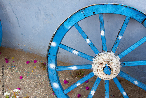 Old wooden blue wheel, close up view of the wheel. The old wooden wheel on the background of the blue wall of the house