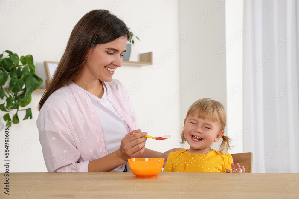 Mother feeding her cute little child with yogurt at wooden table indoors Mother feeding her cute little child with yogurt at wooden table indoors