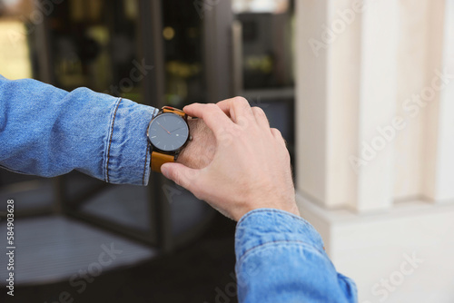 Man looking at watch outdoors, closeup. Being late concept