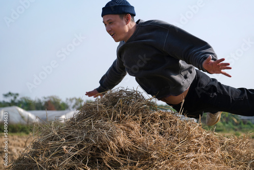 Asian man, jumping and playing on the pile of straw in the rice field