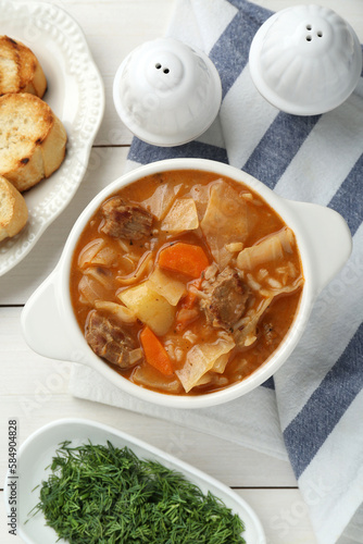 Tasty cabbage soup with meat and carrot served on white wooden table, flat lay