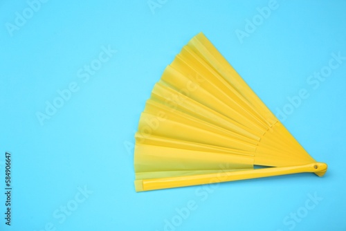 Bright yellow hand fan on light blue background, top view. Space for text