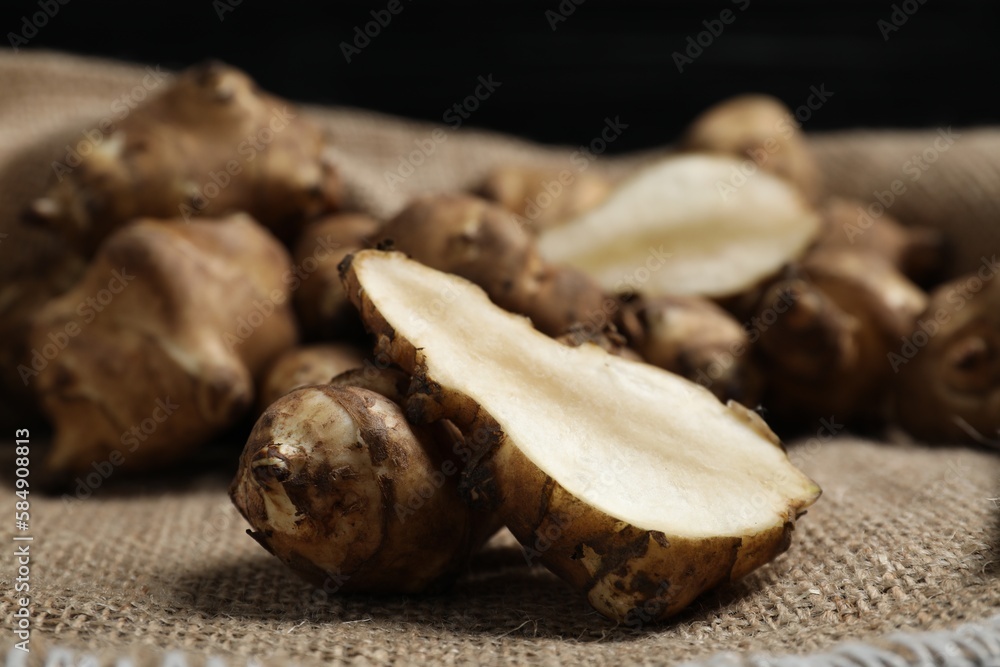 Fototapeta premium Jerusalem artichokes on bag against dark background, closeup
