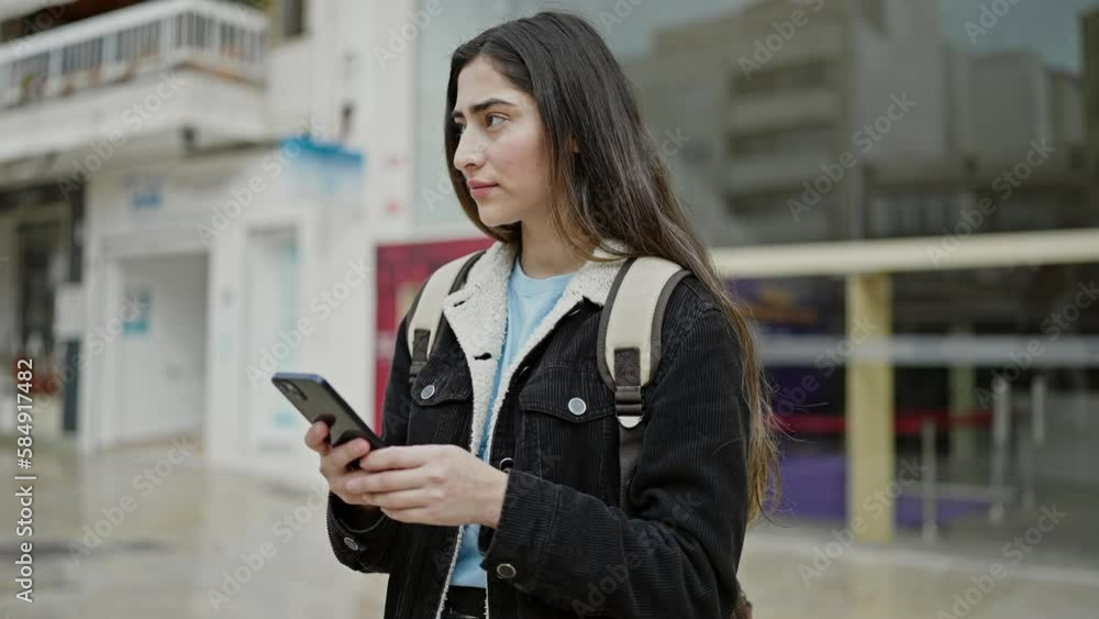 Young beautiful hispanic woman student using smartphone with relaxed expression at street Young beautiful hispanic woman student using smartphone with relaxed expression at street