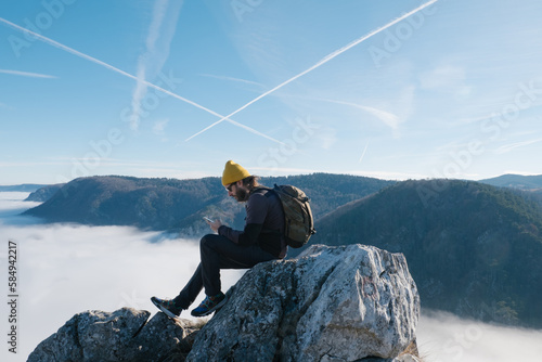 Male Hiker Sitting on Mountain Top While Using Smartphone  photo