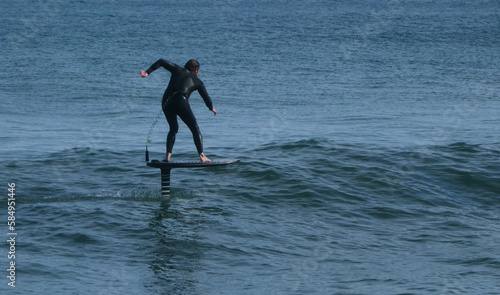 rear view of man wearing wetsuit surfing on hydrofoil board flying over water in ocean photo