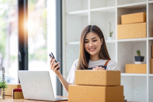 Starting Small business entrepreneur SME freelance, Portrait young woman working at home office, BOX, smartphone, laptop, online, marketing, packaging, delivery, b2b, SME, e-commerce concept.. © wichayada