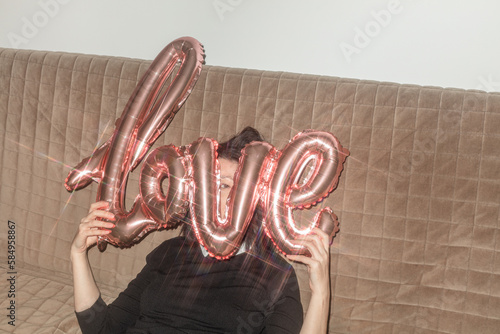 An attractive girl hides and looks out behind a Love balloon