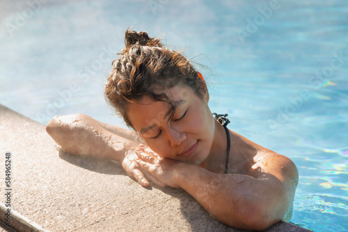 Calm Asian lady relaxing in pool with closed eyes photo