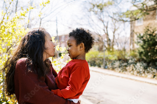 asian mom hugging her son and trying to give him a kiss