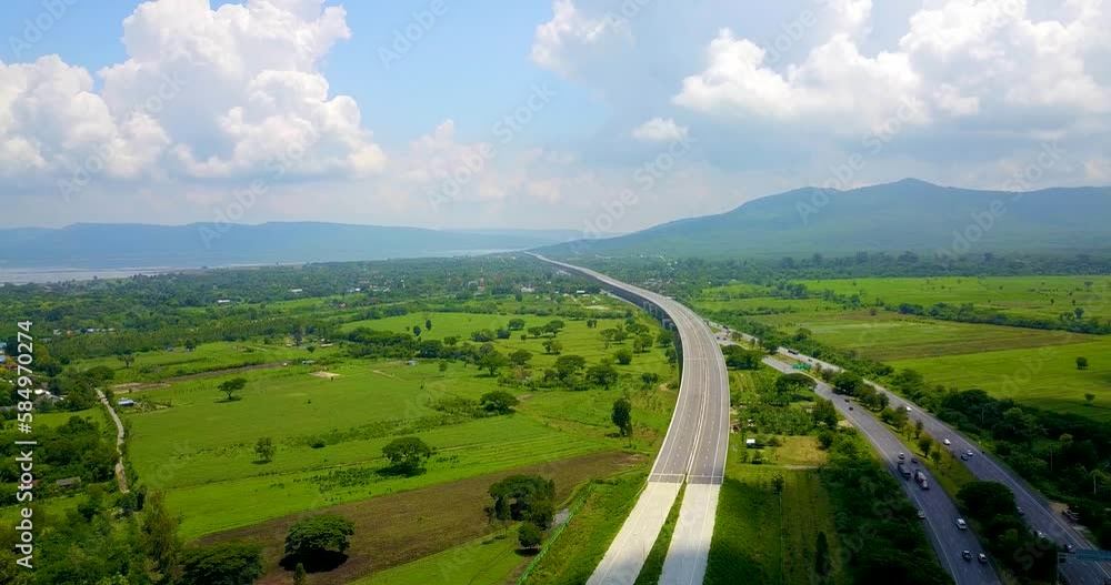 The highway leads into the mountains and green fields side at sunlight with beautiful clouds and blue sky. The highway leads into the mountains and green fields side at sunlight with beautiful clouds and blue sky.