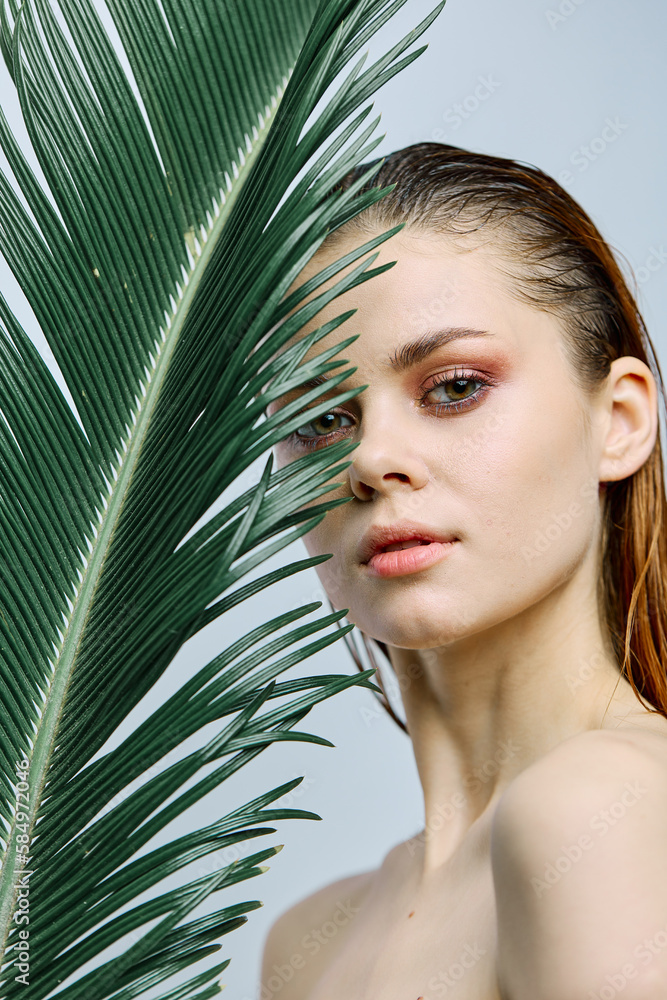 a close beauty portrait of a beautiful woman standing holding a tropical palm leaf in her hand, bringing it to her face. Vertical photo without retouching a close beauty portrait of a beautiful woman standing holding a tropical palm leaf in her hand, bringing it to her face. Vertical photo without retouching