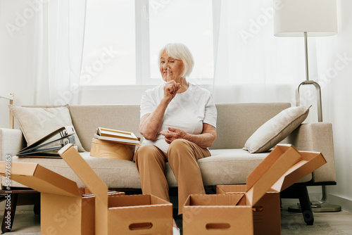 an elderly woman sits on a sofa at home with boxes. collecting things with memories and moving. © SHOTPRIME STUDIO