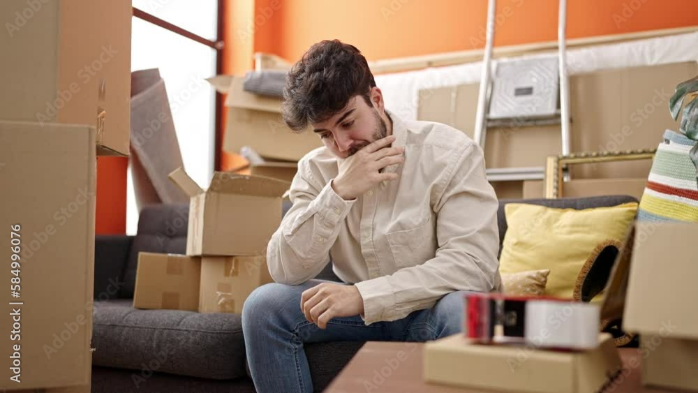 Young hispanic man sitting on sofa with serious expression at new home Young hispanic man sitting on sofa with serious expression at new home