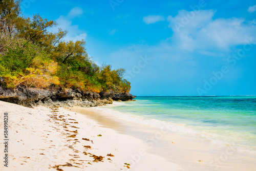 Fototapeta Naklejka Na Ścianę i Meble -  Set against a beautiful blue sky with fluffy clouds on a sunny summer day, Zanzibar Island's tropical beach is a sight to behold. The white sand, palm trees, and crystal-clear turquoise waters combine