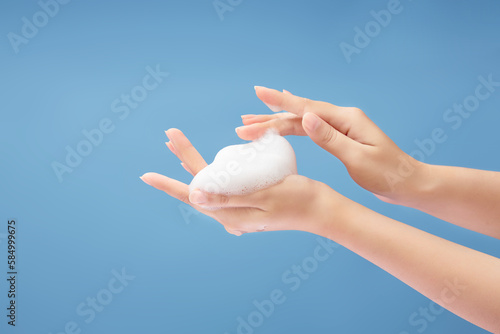 Over a light blue background, a beautiful woman's hands are adorned with white foam mousse. Daily self care routine concept photo