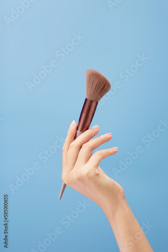 A beautiful hand model is carrying an angled brush over a light blue background. Cosmetic product promotion